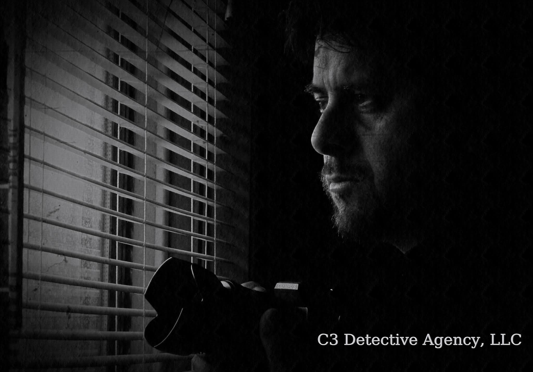 Man peering through window blinds in dramatic black and white, holding a surveillance camera.